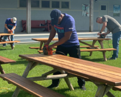 Blue Cross Blue Shield MA volunteers sanding down tables on the island to help prepare for the 2021 camp season